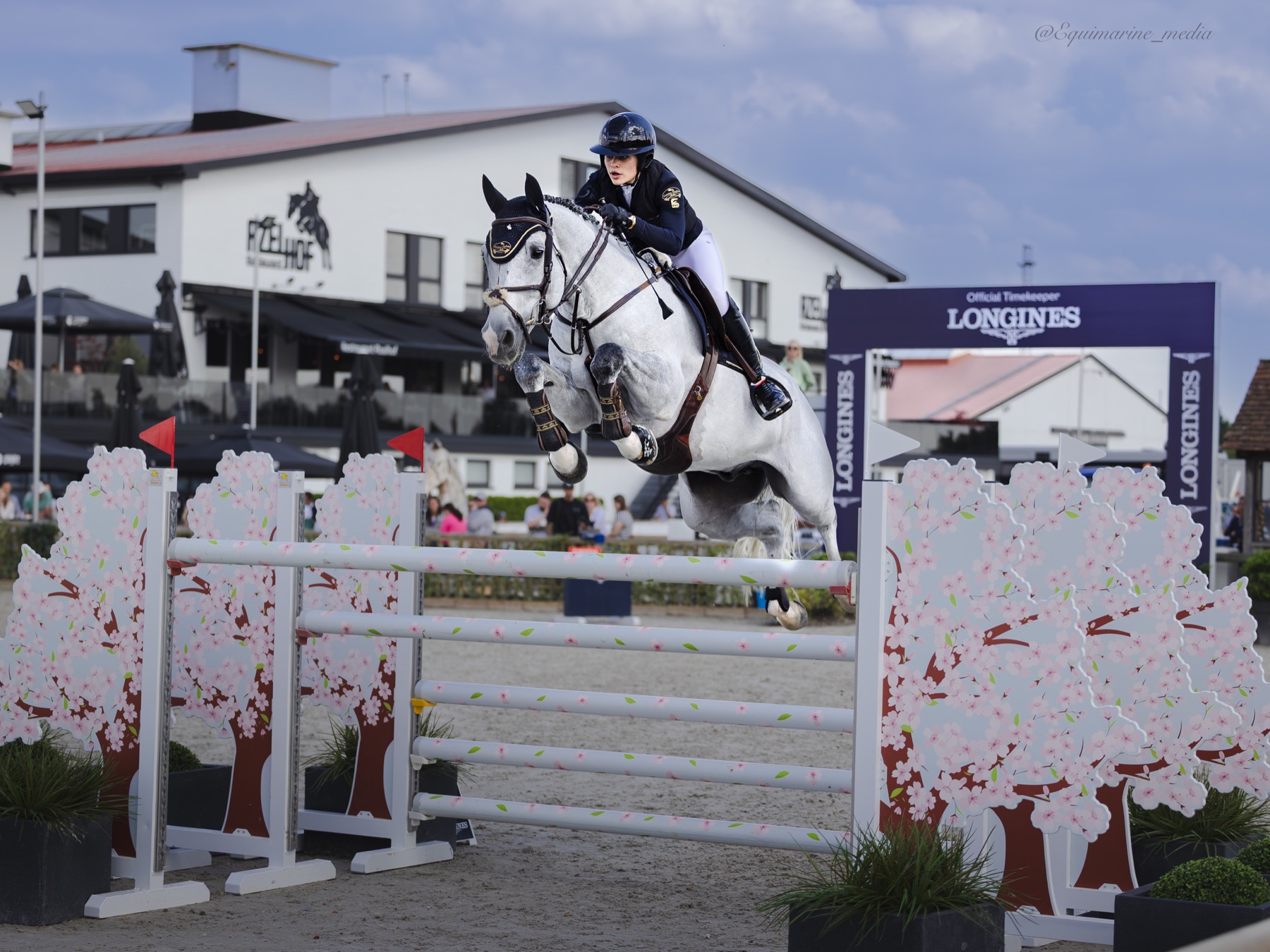 Emma Sophia Španko na koni přeskakuje překážku zdobenou třešňovými květy na parkurovém závodě pod záštitou Longines
