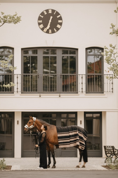 A groom with a blanketed horse before the manor balcony