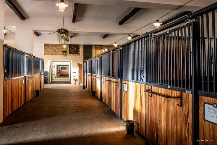 Stable aisle with wood-beam ceiling and a wall clock