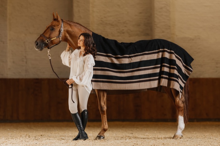 A rider with her blanketed horse in the indoor arena